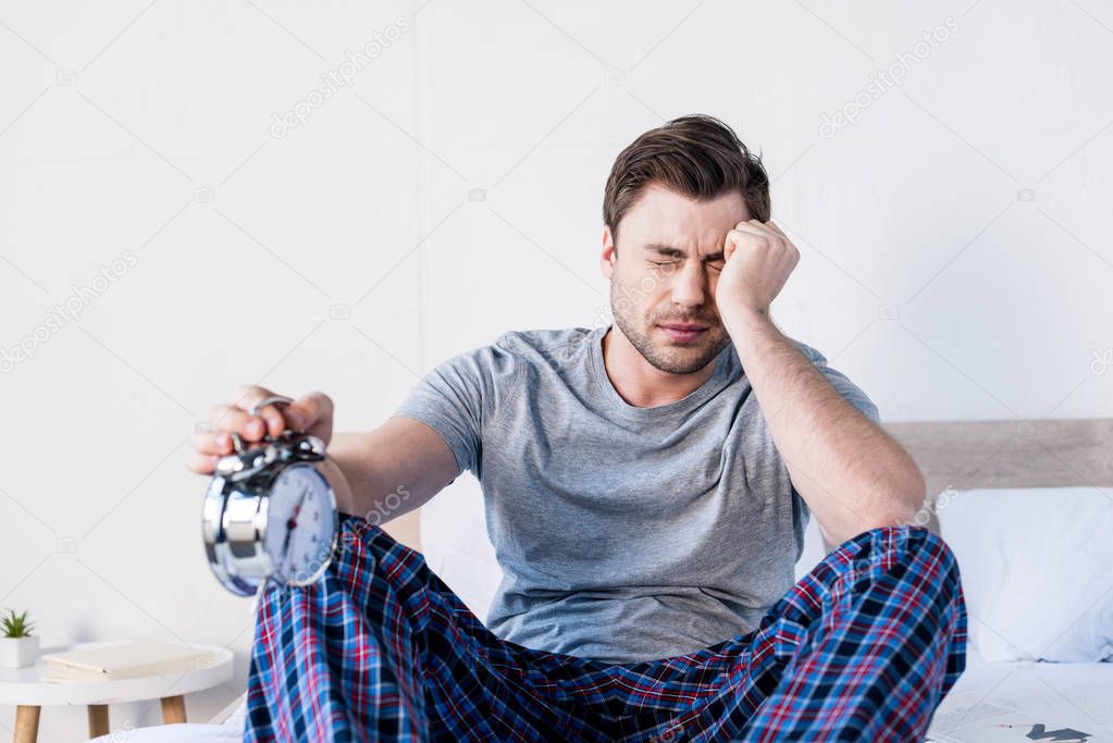 selective focus of handsome overslept man with closed eyes holding alarm clock