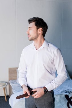 Yatak odasında kendine güvenen yakışıklı adam soyunma ve uzakta bakıyor
