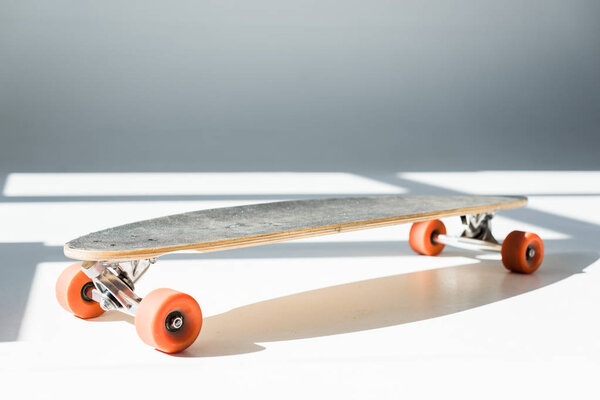 selective focus of longboard in sunlight with shadows on grey 