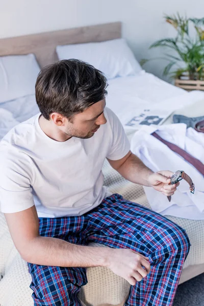 Handsome Man Pyjamas Holding Watch While Sitting Bedding Home — Stock Photo, Image