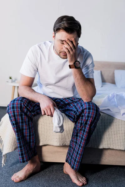 Schöner Schläfriger Mann Sitzt Auf Bettwäsche Und Hält Weiße Socken — Stockfoto