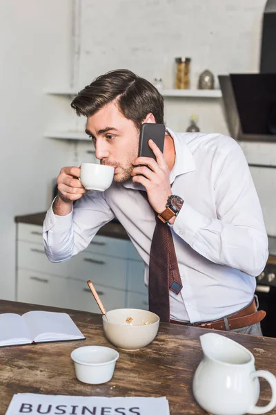 Dobrze Wyglądający Człowiek Picia Kawy Rozmawiać Smartphone Kuchni Domu — Zdjęcie stockowe