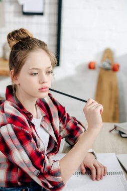 Ev ödevi yaparken damalı gömlek masada kalem tutan Pensive genç