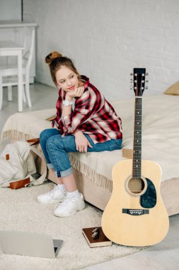Neşeli genç yatakta oturan ve akustik gitar bakıyor