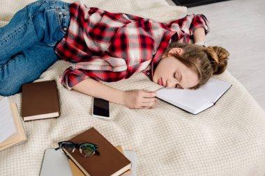 Genç içinde damalı gömlek Sleeping üzerinde yatak ile kitap ve Smartphone