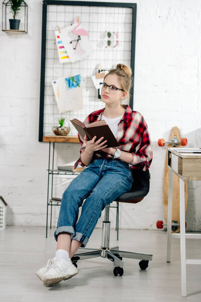 Curious teenage kid in glasses and checkered shirt reading book