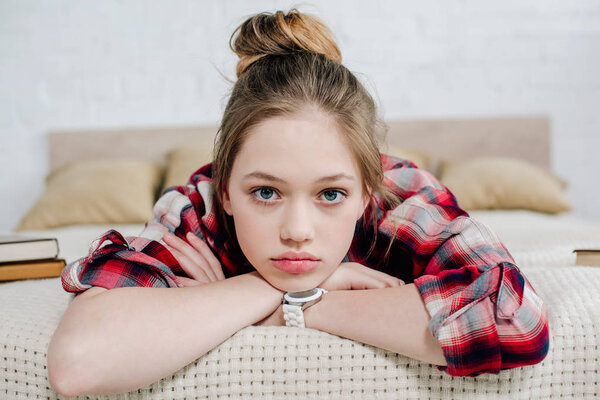Front view of teenager kid in wristwatch lying on bed and looking at camera