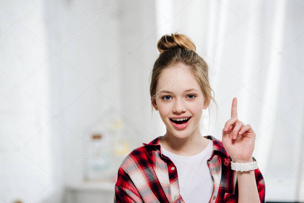 Front view of excited teenage kid in checkered shirt showing idea sign