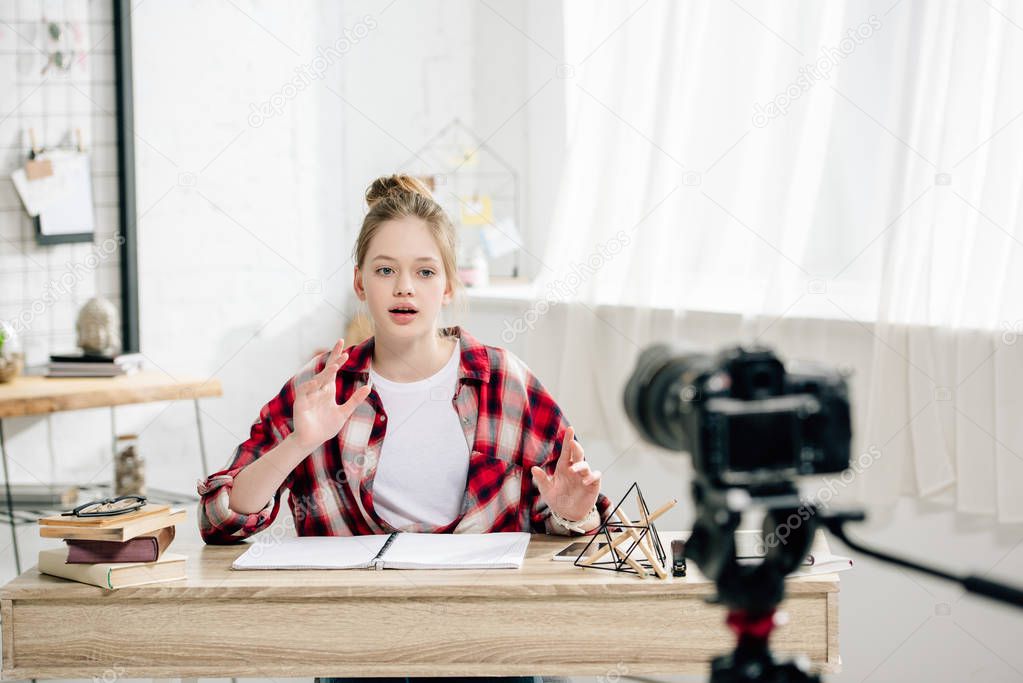 Teenage blogger sitting at desk in front of video camera and making video