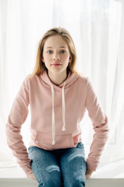 Pencere eşik oturan ve kamera bakarak pembe hoodie genç çocuğun ön görünümü