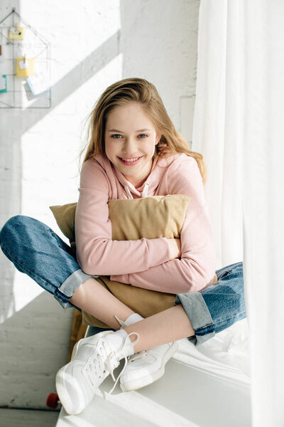 Smiling teenage kid embracing brown cushion and looking at camera