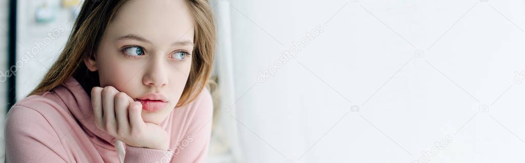 Panoramic shot of teenager propping face with hand and looking away