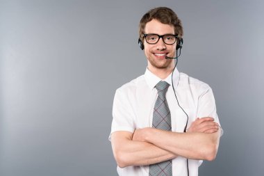 smiling call center operator in glasses and headset with crossed arms on grey background clipart