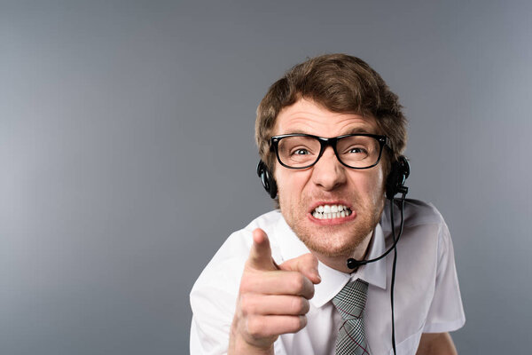 irritated call center operator in headset and glasses pointing with finger at camera