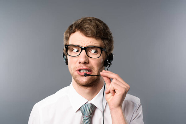 путаница оператора колл-центра в гарнитуре и очках, глядя в сторону на сером фоне
