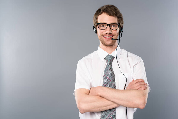 smiling call center operator in glasses and headset with crossed arms on grey background