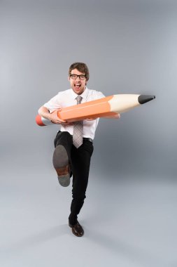 funny busines man in glasses holding huge decorative pencil, screaming and marching on grey background clipart