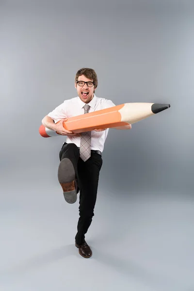stock image funny busines man in glasses holding huge decorative pencil, screaming and marching on grey background