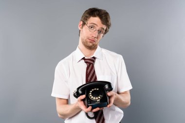 sad businessman in glasses holding vintage phone on grey background clipart