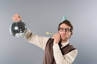 parlak disko topu tutarak ve gri arka plan üzerinde parti boynuz üfleme parti şapkalı heyecanlı adam