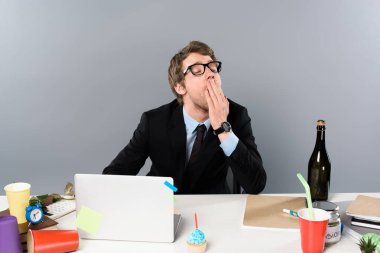 businessman yawing at workplace near cupcake and paper cups isolated on grey clipart