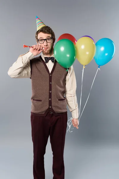 メガネと灰色の背景に色とりどりの風船とパーティー ホーンを保持パーティー キャップで変な男 — ストック写真