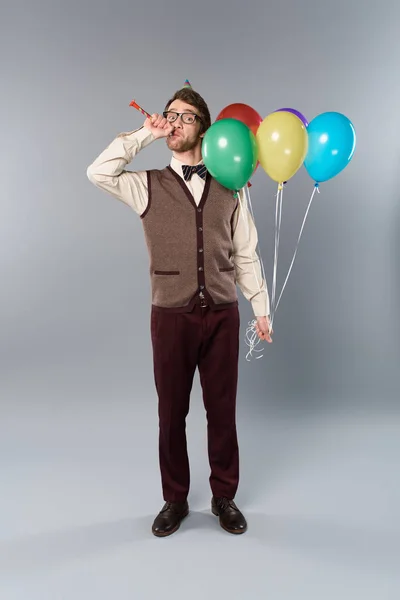 メガネと色とりどりの風船を押し 灰色の背景に党ホルン吹いてパーティー キャップの男 — ストック写真