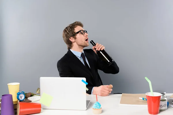 Businessman Sitting Workplace Cupcake Drinking Champagne Bottle Isolated Grey — Stock Photo, Image