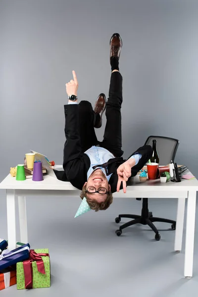 Happy Businessman Party Cap Lying Table Messy Workplace Showing Peace — Stock Photo, Image