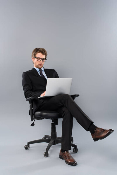 businessman in suit sitting in chair and using laptop on grey background
