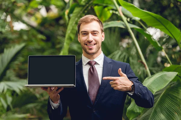 Smiling Businessman Suit Tie Pointing Finger Laptop Blank Screen Orangery — Stock Photo, Image