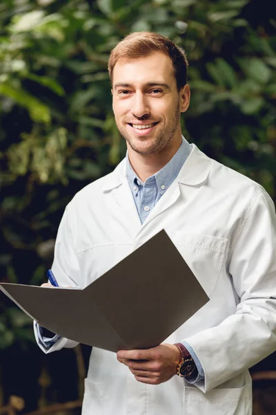 Smiling Scientist White Coat Holding Journal Green Orangery — Stock Photo, Image