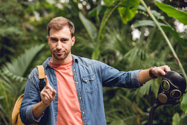traveler with backpack pointing at gas mask in tropical forest