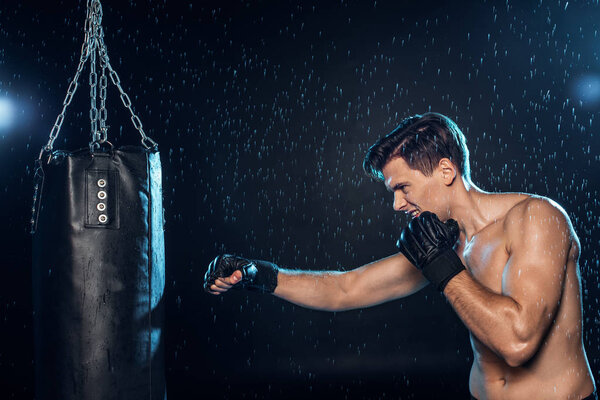 Boxer training with punching bag under water drops on black