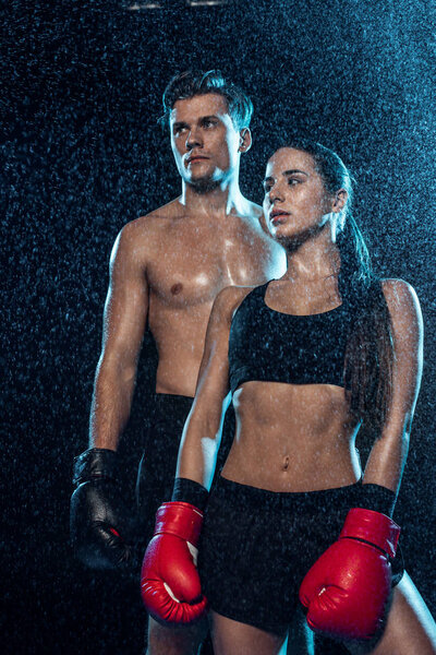 Два боксера в боксерских перчатках стоят под каплями воды и смотрят в сторону черного
