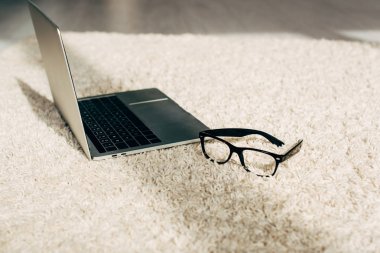 Güneşte odada halı üzerinde gözlük yakın modern laptop 