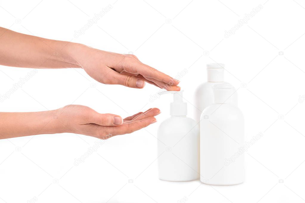 Partial view of girl with cosmetic bottles applying cream isolated on white