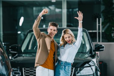 cheerful man standing with excited blonde girl gesturing and screaming near car  clipart
