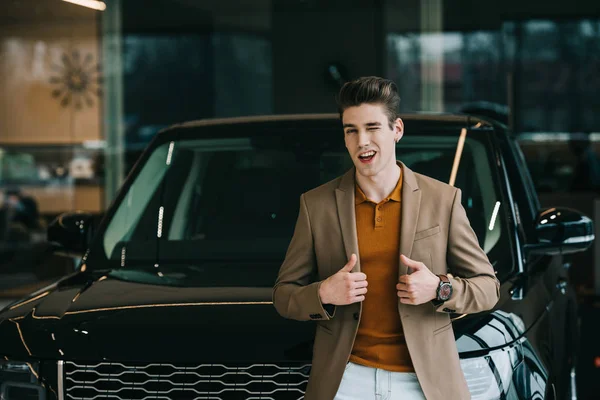 Fröhlicher Mann Steht Neben Auto Autohaus Und Zeigt Daumen Hoch — Stockfoto