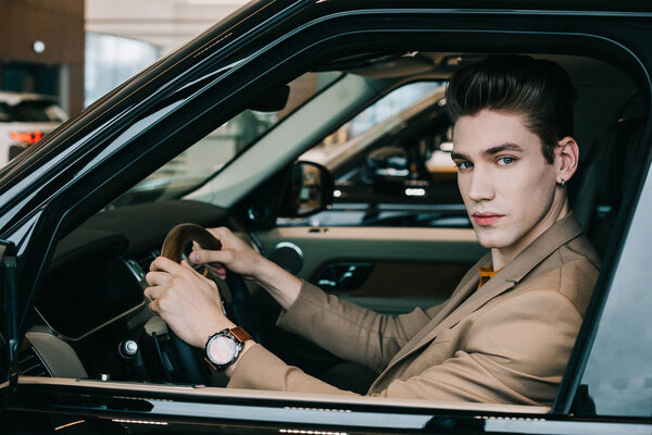 handsome man holding steering wheel and looking at camera 