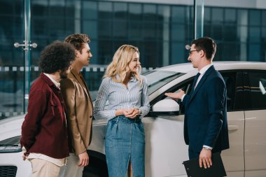Araba showroom neşeli arkadaşlar yakınında ayakta iken yakışıklı araba bayi işaret 