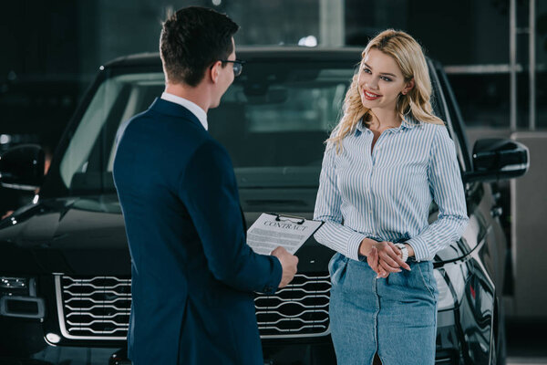 car dealer holding clipboard with contract near attractive blonde woman 