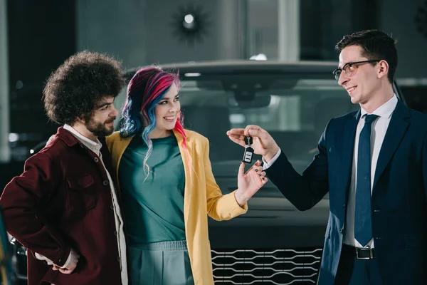 Wesoły Sprzedawca Samochodów Okularach Dając Klucz Kobiety Kolorowymi Włosami Mężczyzną — Zdjęcie stockowe