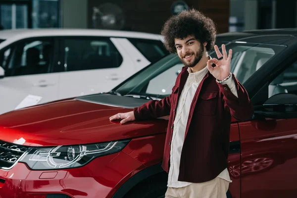 Cheerful Curly Man Showing Sign While Standing Red Car — Stock Photo, Image