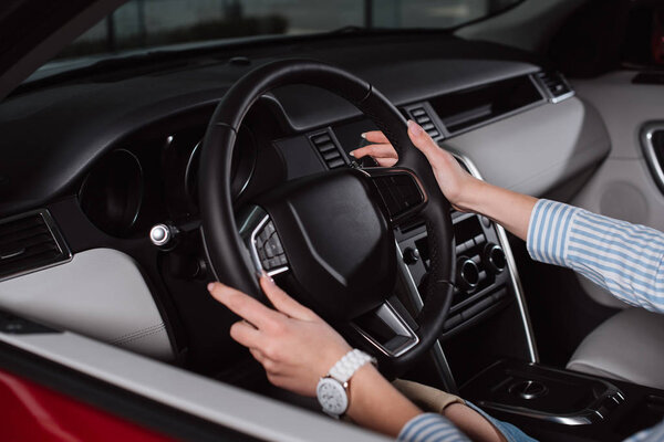 cropped view of young woman holding steering wheel while sitting in car 