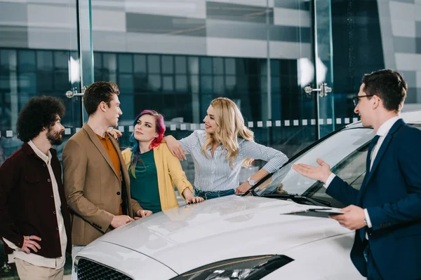 Car Dealer Glasses Gesturing While Looking Cheerful Friends White Car — Stock Photo, Image