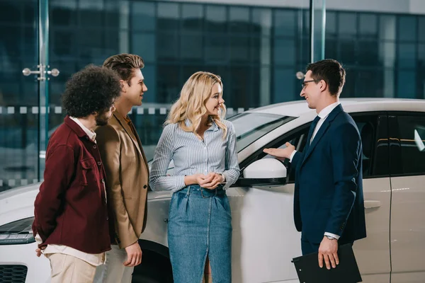 Handsome Car Dealer Gesturing While Standing Cheerful Friends Car Showroom — Stock Photo, Image