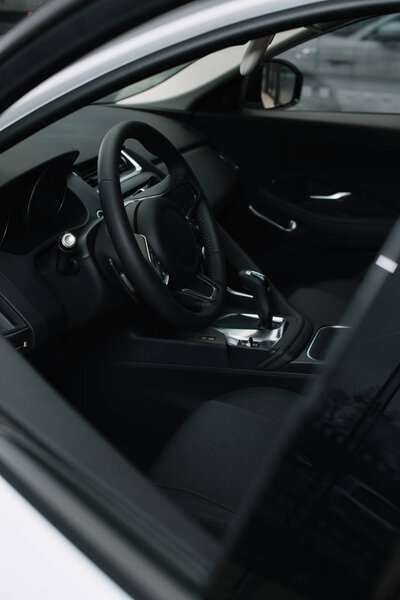 selective focus of black steering wheel near gear shift handle in luxury car 