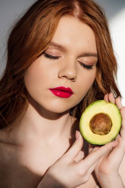 Kırmızı dudaklar ve gözleri ile güzel Redhead kız kesilmiş avokado ile poz kapalı