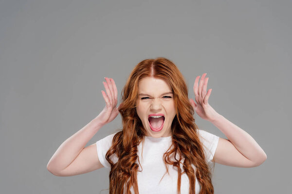 beautiful redhead girl looking at camera, gesturing with hands and yelling isolated on grey